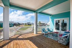 A covered porch with a hammock, two chairs, and a table. - Large & Glam~ sleeps16~ waterfront~ VIEWS~ fenced ~ BEACH ACCESS ~DOG (Bolivar Peninsula)