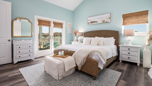 Quarto com uma cama grande, penteadeira, mesa de cabeceira e janela com persianas.