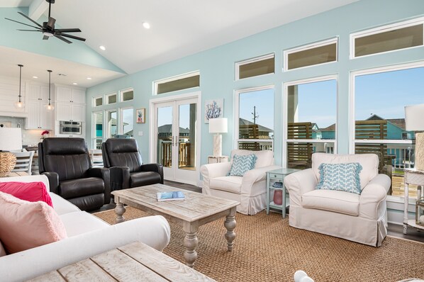 A spacious living room with a high ceiling, large windows, and a ceiling fan. - Large & Glam~ sleeps16~ waterfront~ VIEWS~ fenced ~ BEACH ACCESS ~DOG (Bolivar Peninsula)