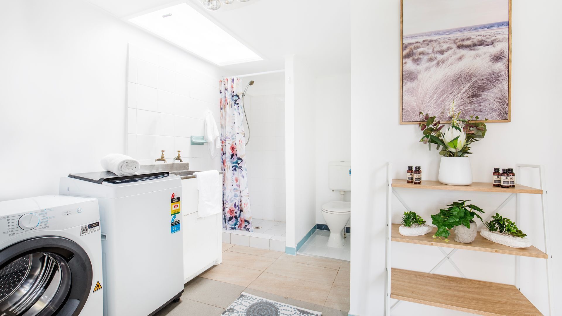 A modern laundry room with a washing machine, dryer, and a shower area.
