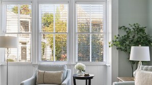 A living room with a grey sofa, a round coffee table with decorative items, a floor lamp, and a window with blinds. - Pet-Friendly +Historic Charm & Modern Comfort Near Upper King (Charleston)