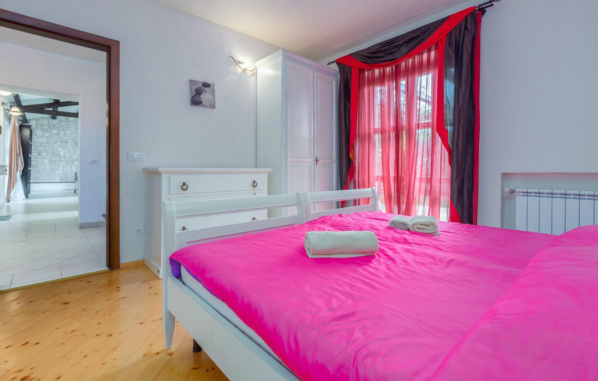 A bedroom with a bed, a dresser, a mirror, and a window with curtains.
