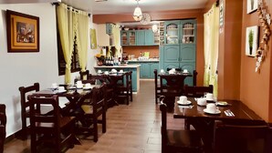 Comedor con mesas y sillas de madera, cocina al fondo y un cartel que indica la sala de comidas.