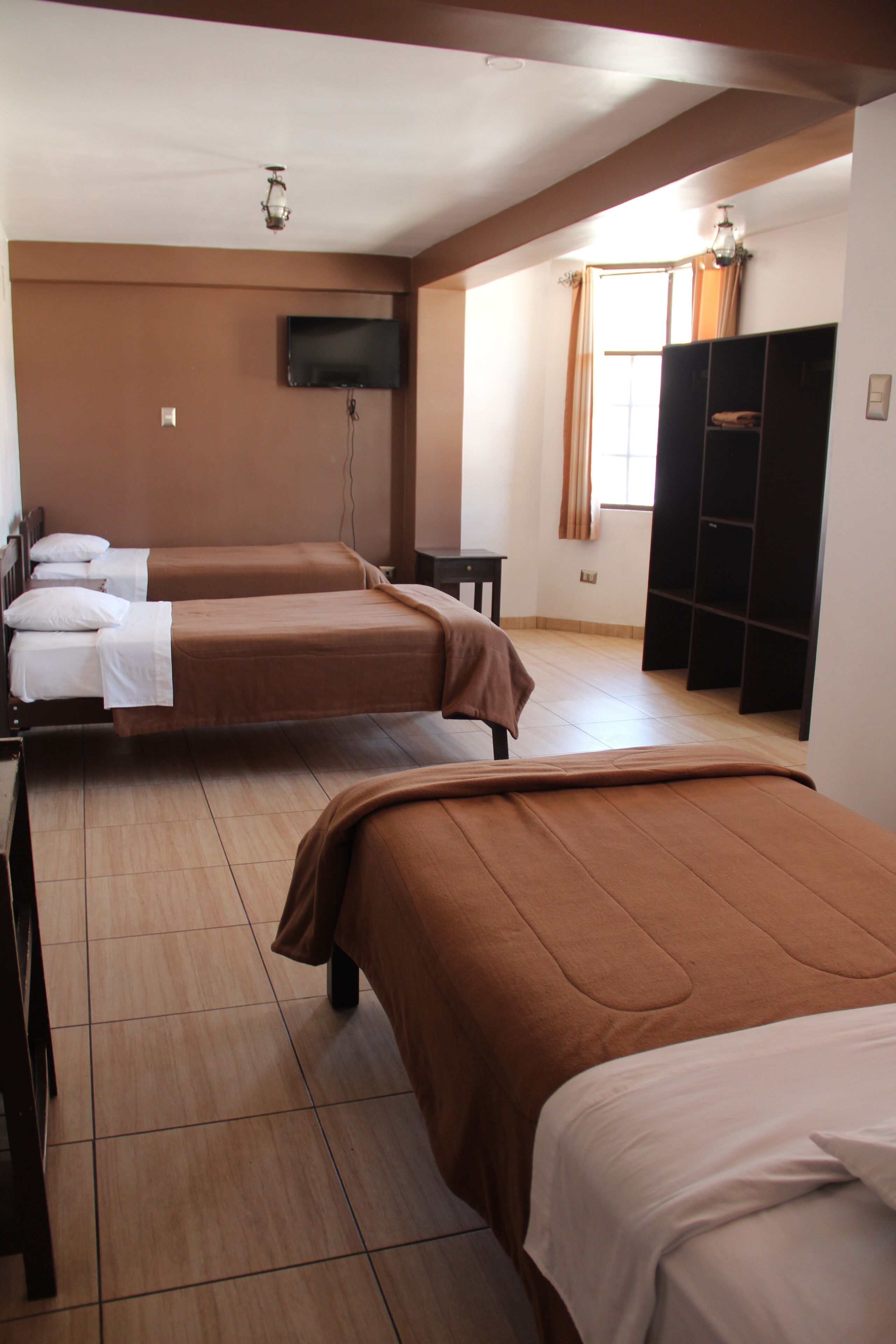 A hotel room with two beds, a TV mounted on the wall, and a wardrobe.