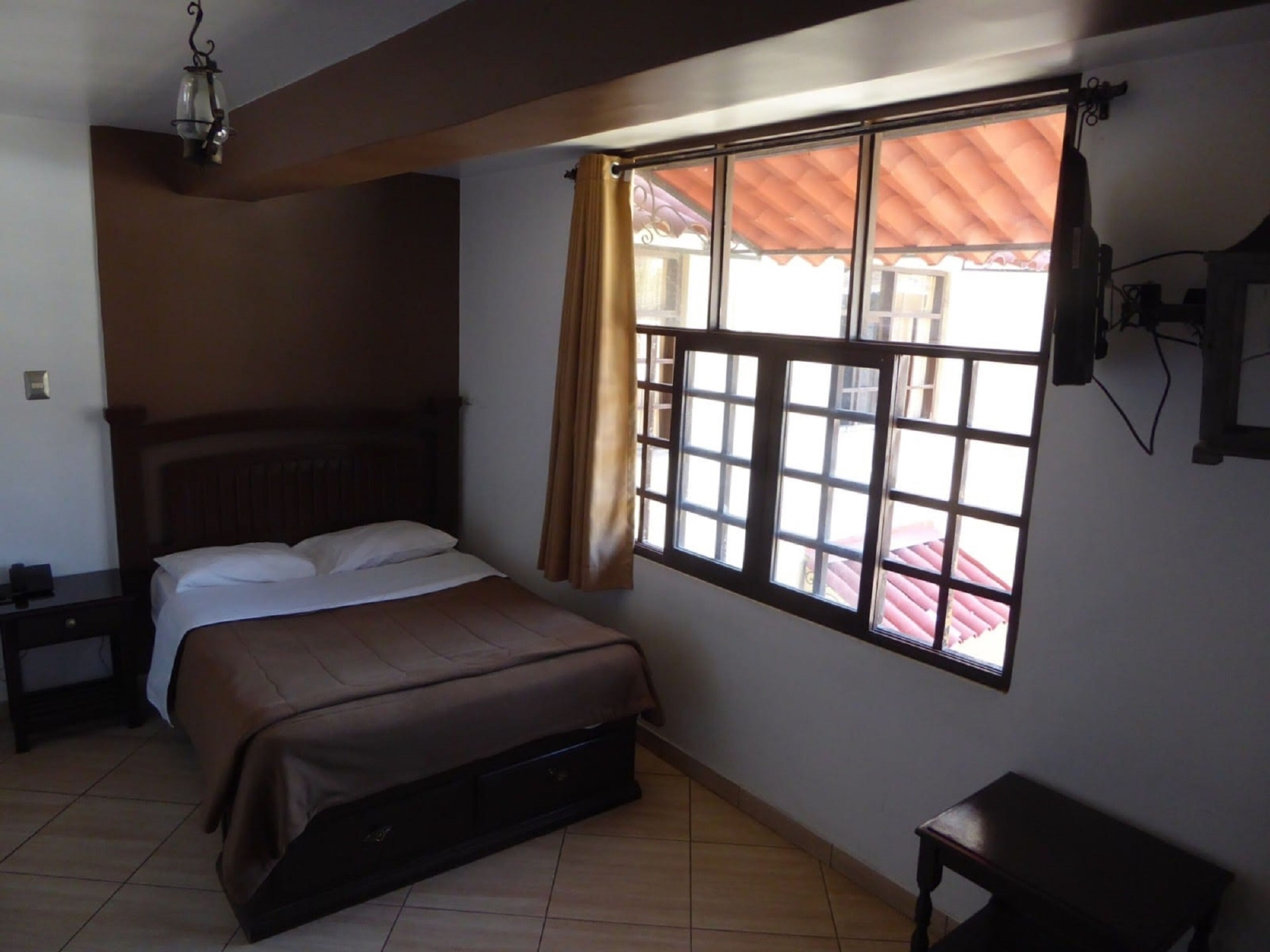 A bedroom with a bed, a nightstand, a window with curtains, and a ceiling light fixture.