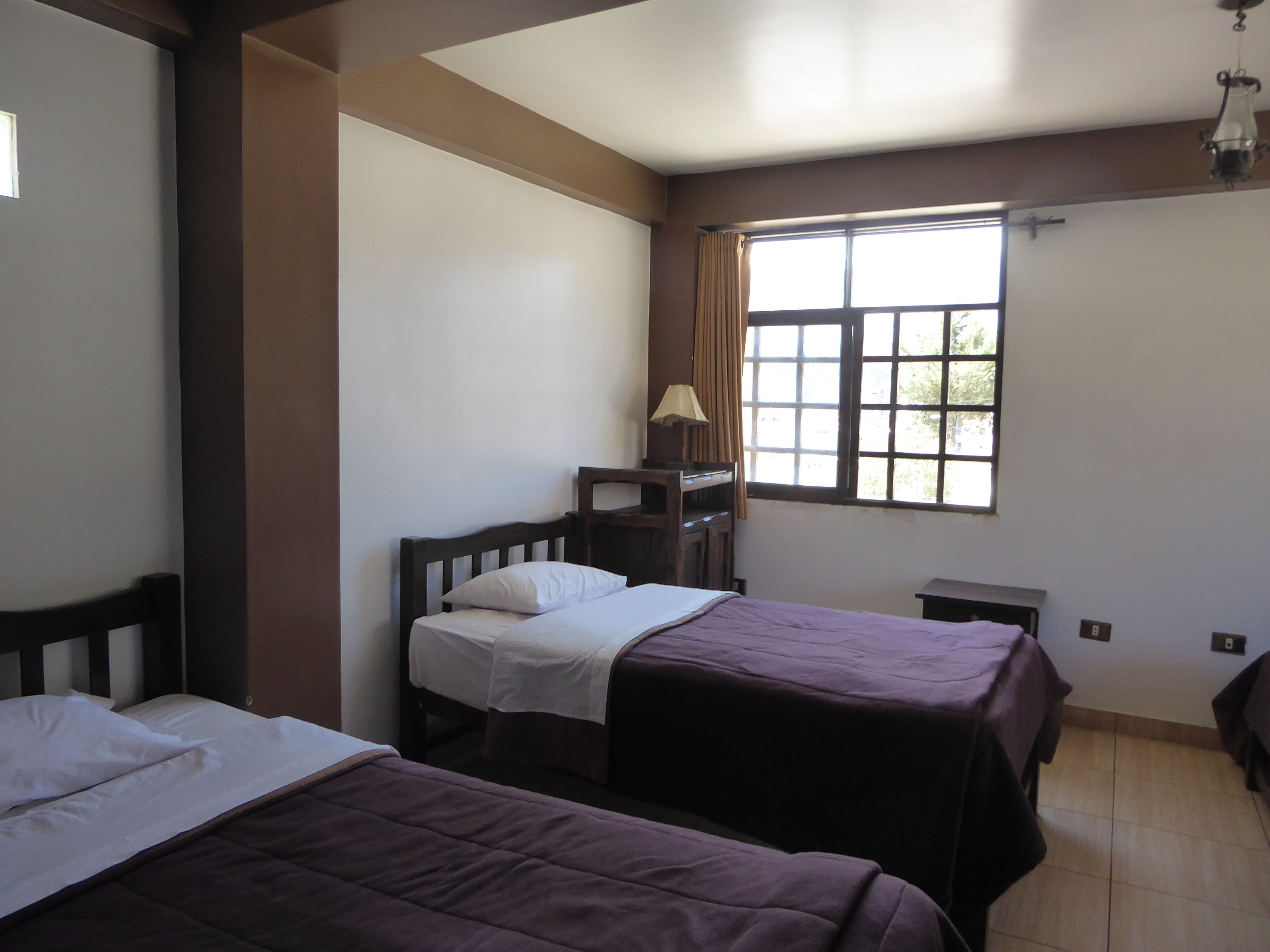 A room with two beds, a window with curtains, a desk, and a lamp.
