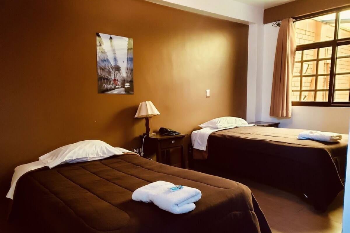 A hotel room with two beds, a lamp, a painting, and a window with curtains.