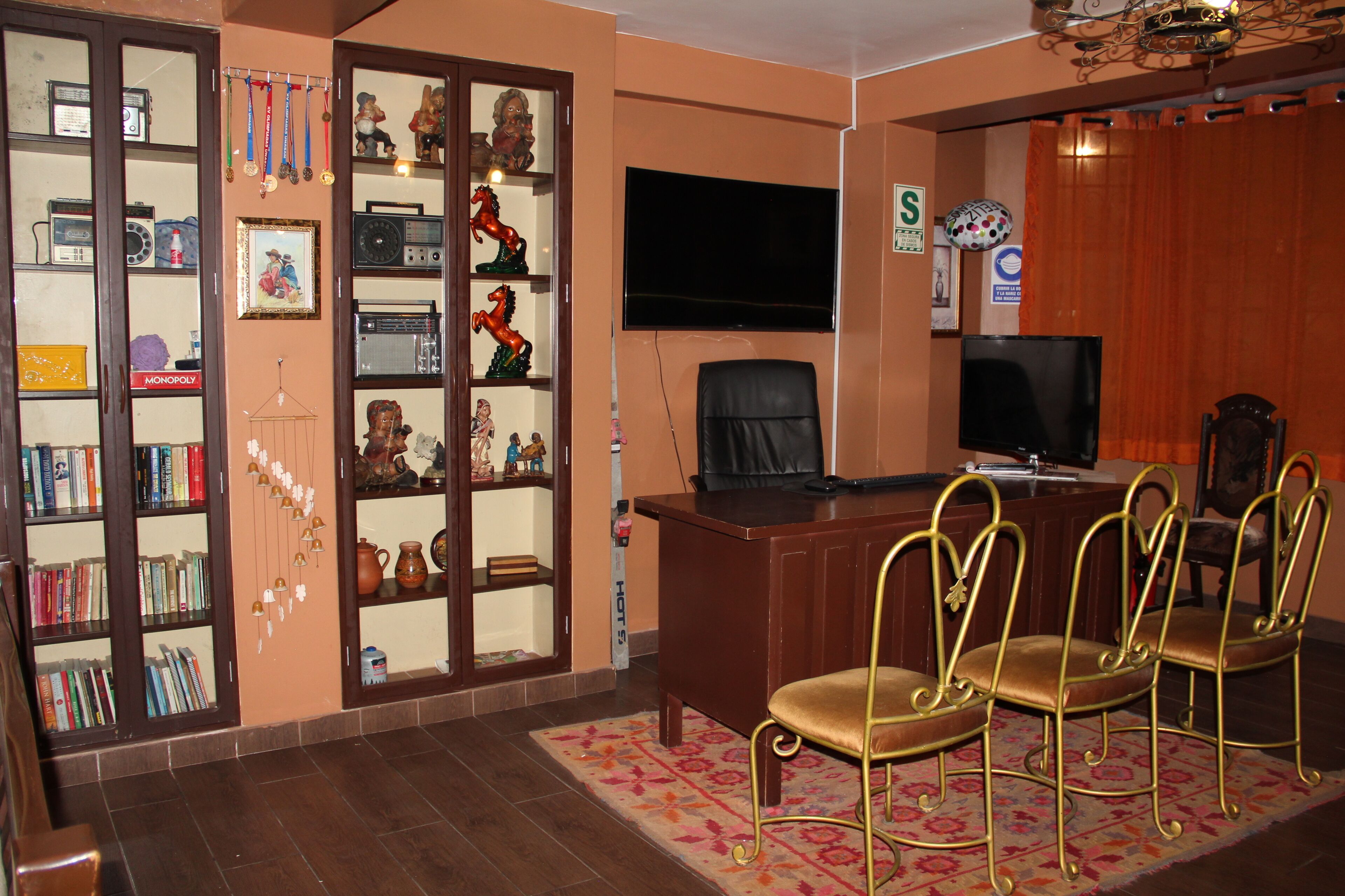 Una habitación con un escritorio, un televisor y una estantería llena de libros y objetos decorativos.
