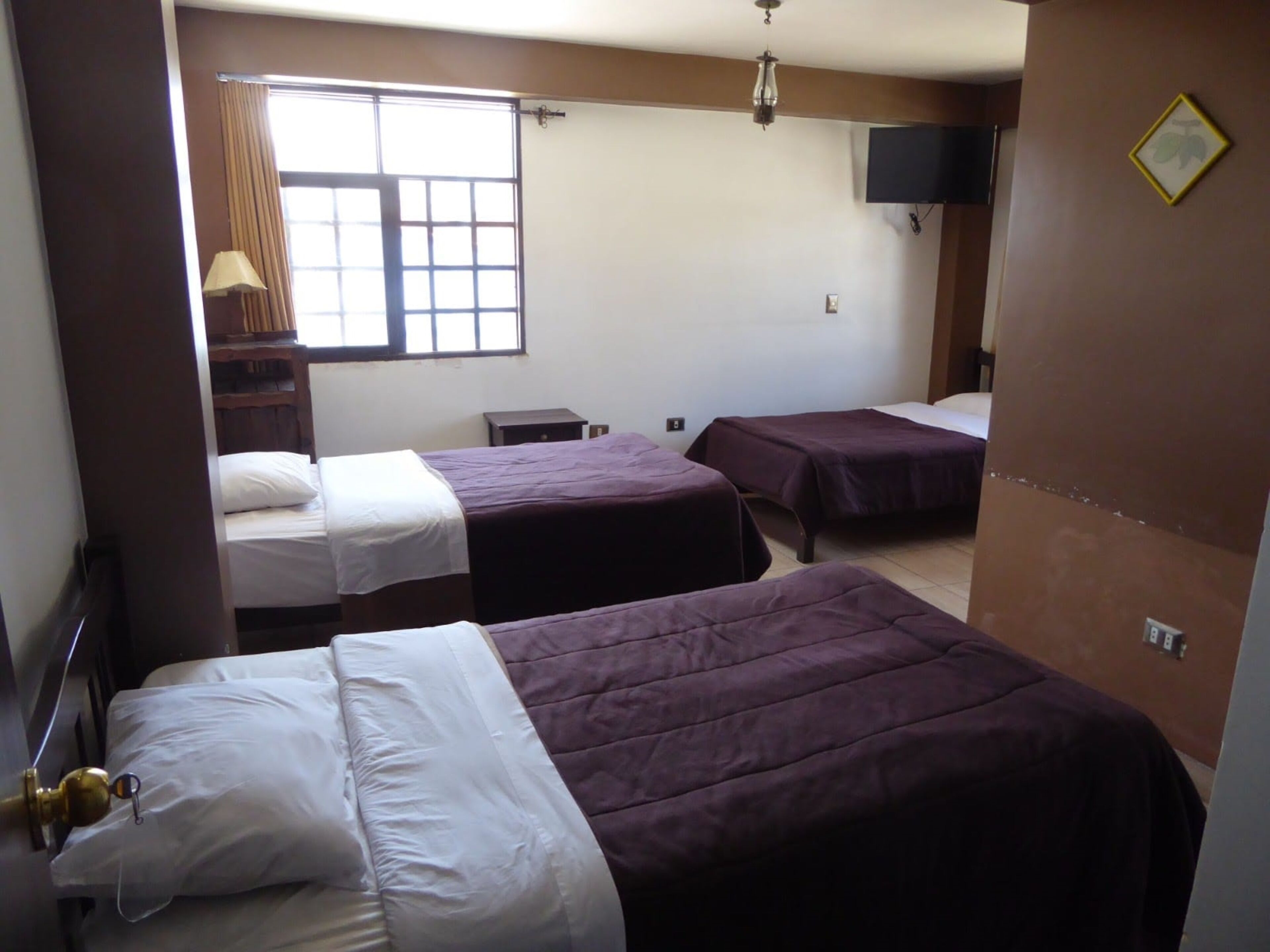 A hotel room with two beds, a window with curtains, a TV mounted on the wall, and a small table.