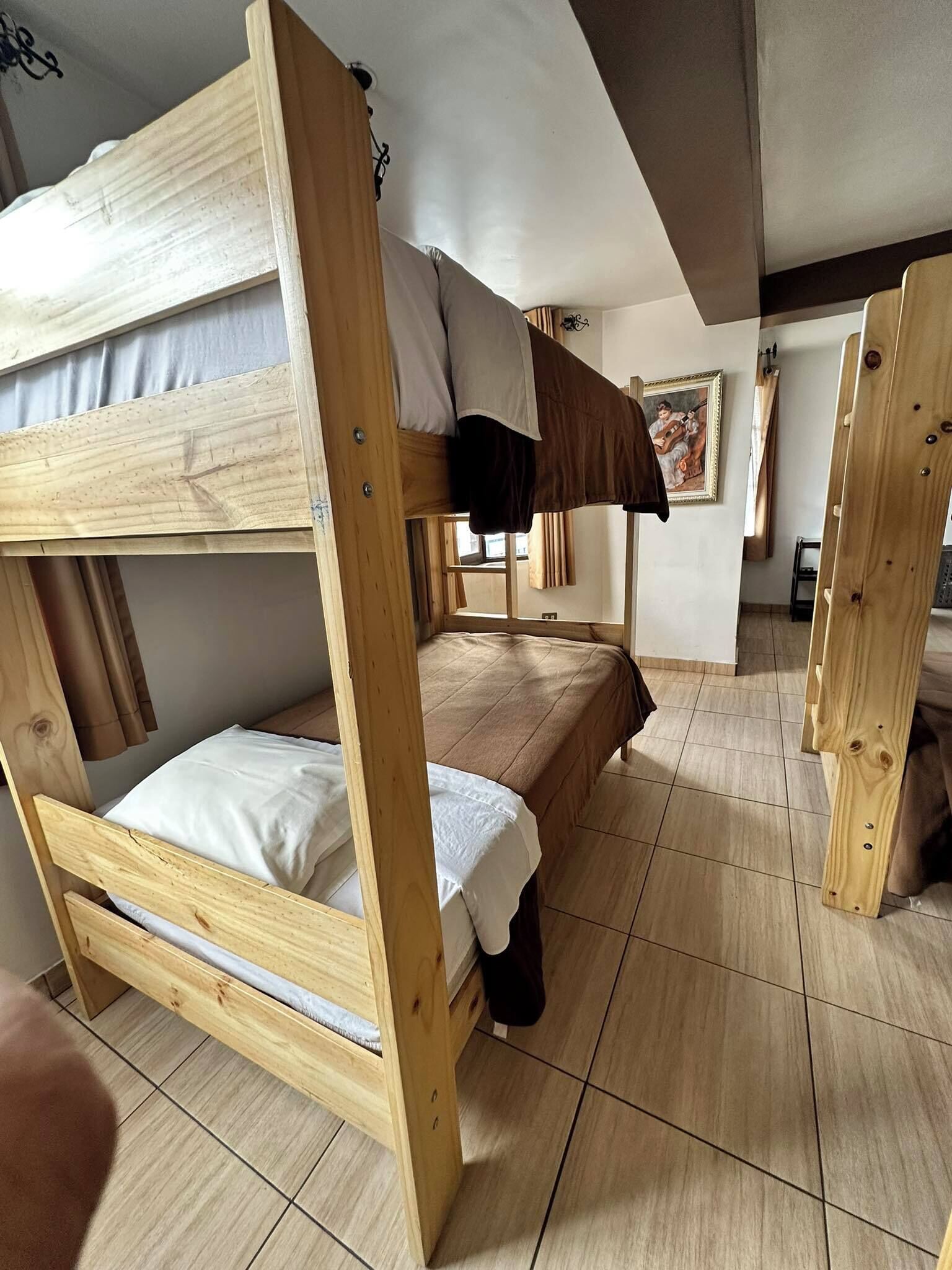 Une chambre avec un lit superposé en bois, une fenêtre et un tableau accroché au mur.
