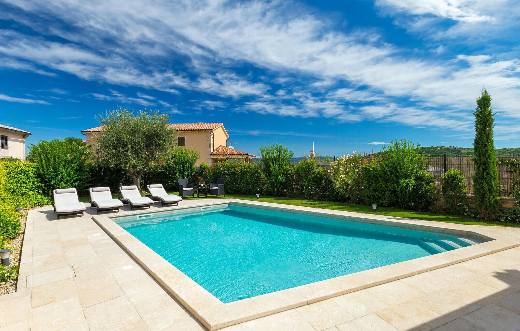 A rectangular swimming pool with a tiled deck, surrounded by lounge chairs and greenery.