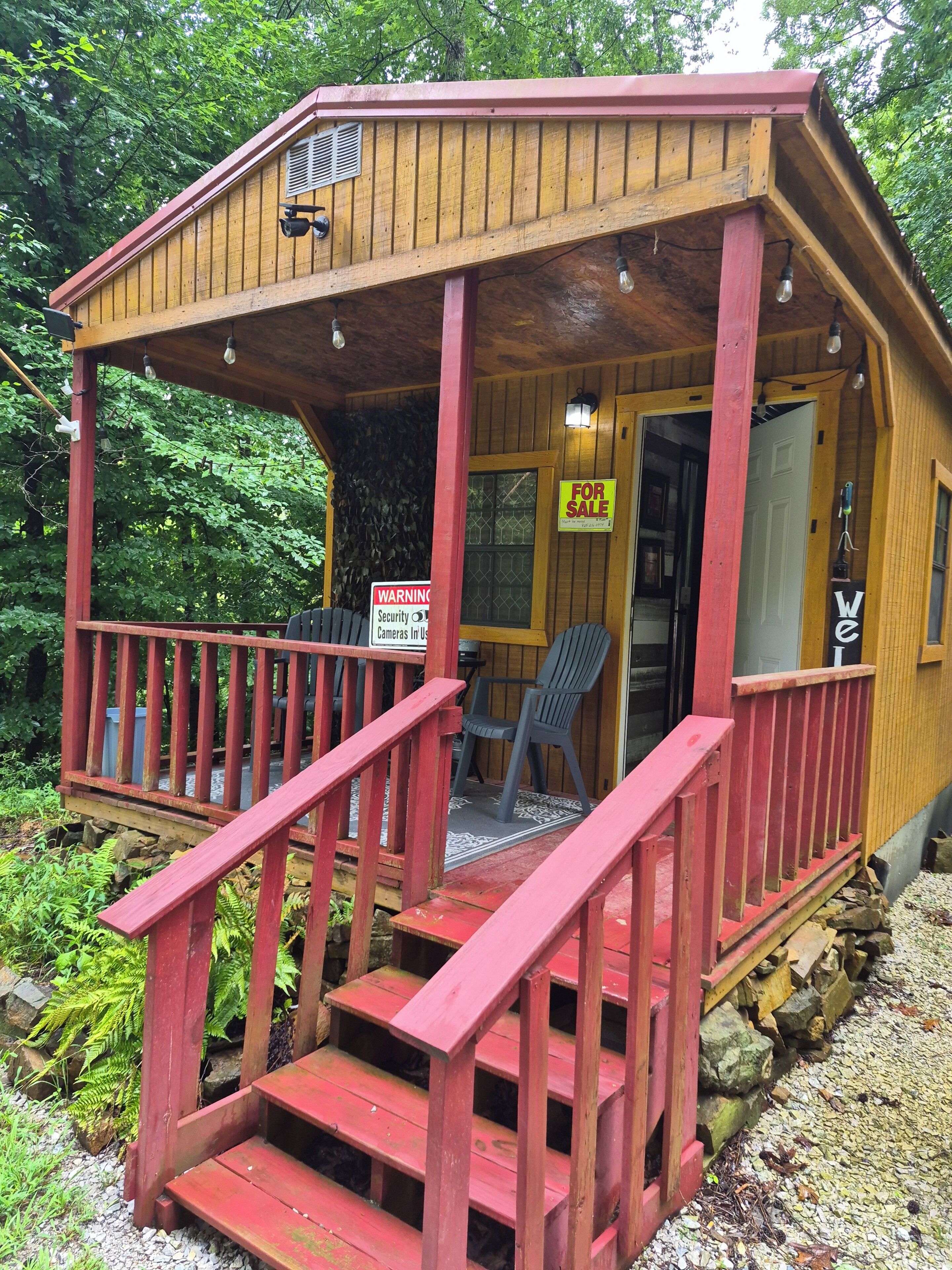 Une cabane en bois avec une véranda, des marches et une pancarte « À vendre ».