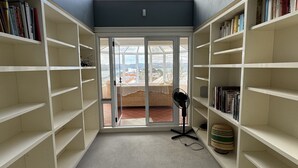 Ett bibliotek med bokhyllor på båda sidor, en fläkt och en utsikt genom en glasdörr ut mot omvärlden.