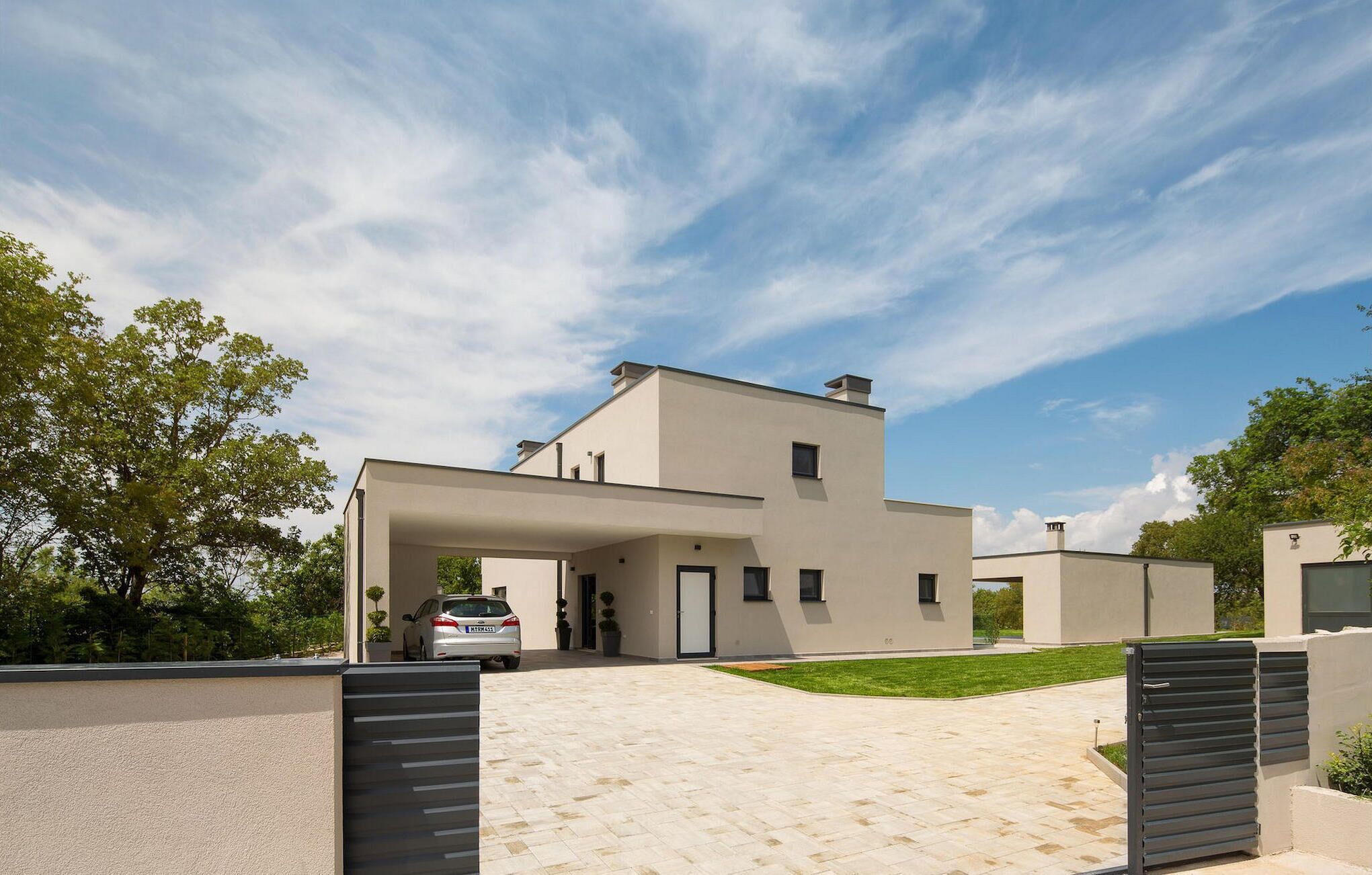 A modern two-story house with a covered driveway, a car parked in the driveway, and a well-maintained lawn.