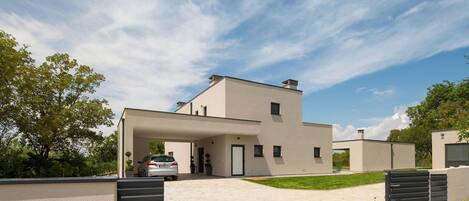 A modern two-story house with a covered driveway, a car parked in the driveway, and a well-maintained lawn.