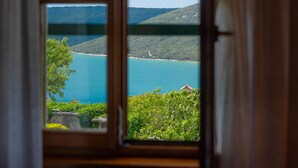 Vista desde una ventana que muestra un paisaje costero con una masa de agua, vegetación y una colina distante.
