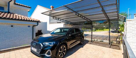 A black SUV parked under a covered parking area with a clear blue sky.