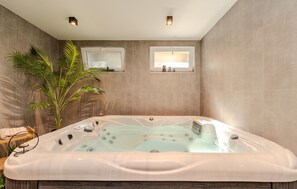 A modern bathroom with a large bathtub, a potted plant, and a small window.