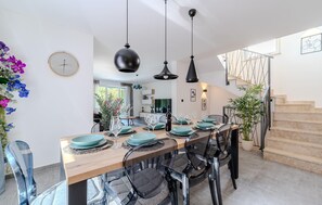 Un coin repas avec une table en bois dressée pour quatre personnes, des chaises noires et des luminaires suspendus.
