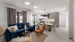 Un soggiorno moderno con un divano blu, un'area pranzo con tavolo e sedie, e una cucina sullo sfondo.