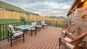 Una terraza con mesa y sillas de vidrio, rodeada por una valla de madera y vistas a un paisaje montañoso.