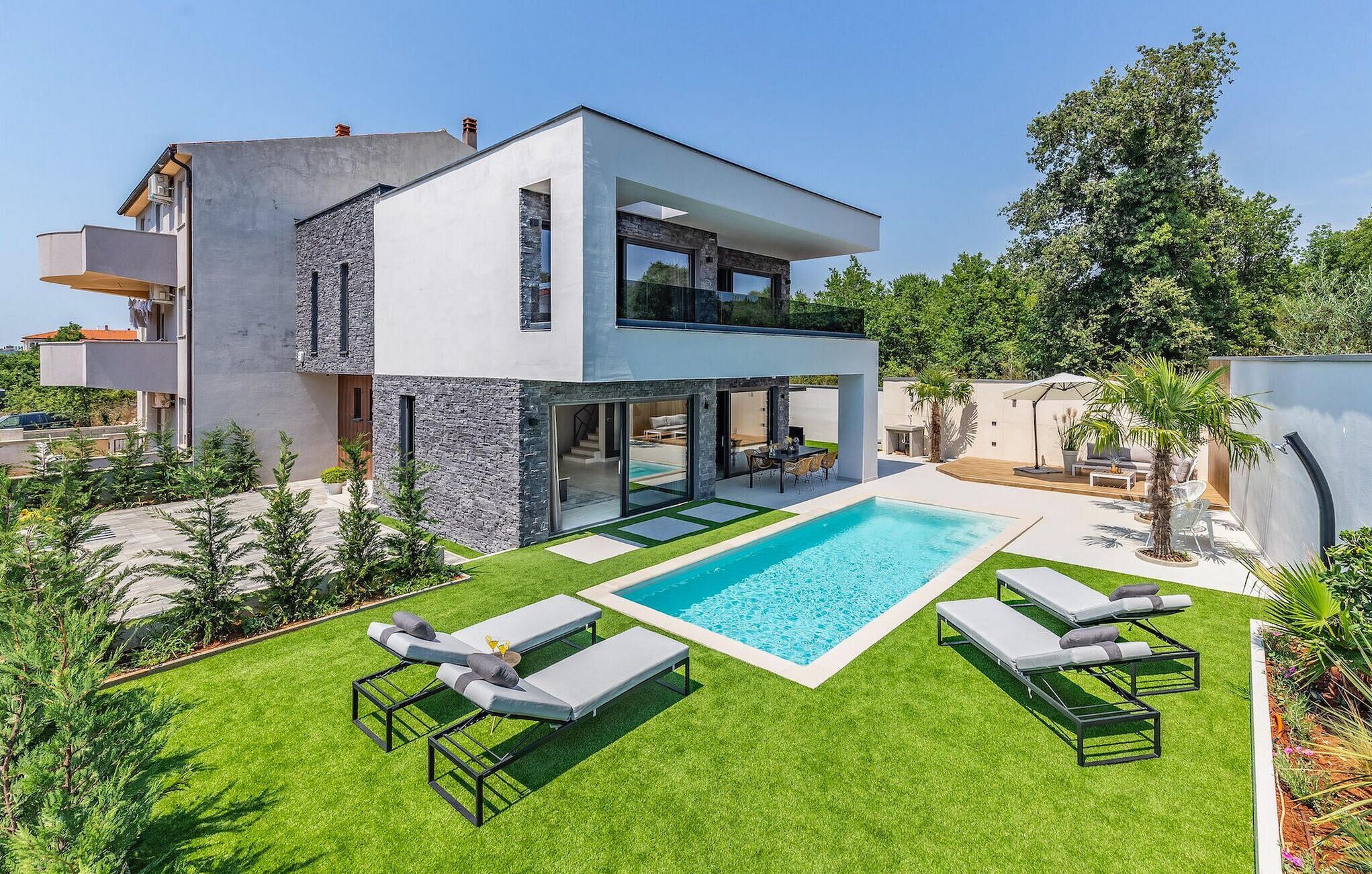 A modern two-story house with a swimming pool, outdoor seating, and a well-maintained lawn.