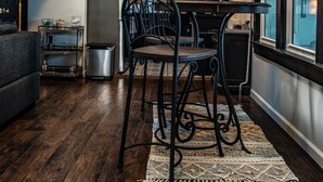 Een moderne keuken met donkere houten vloeren, een eethoek met metalen stoelen en een uitzicht door een raam.