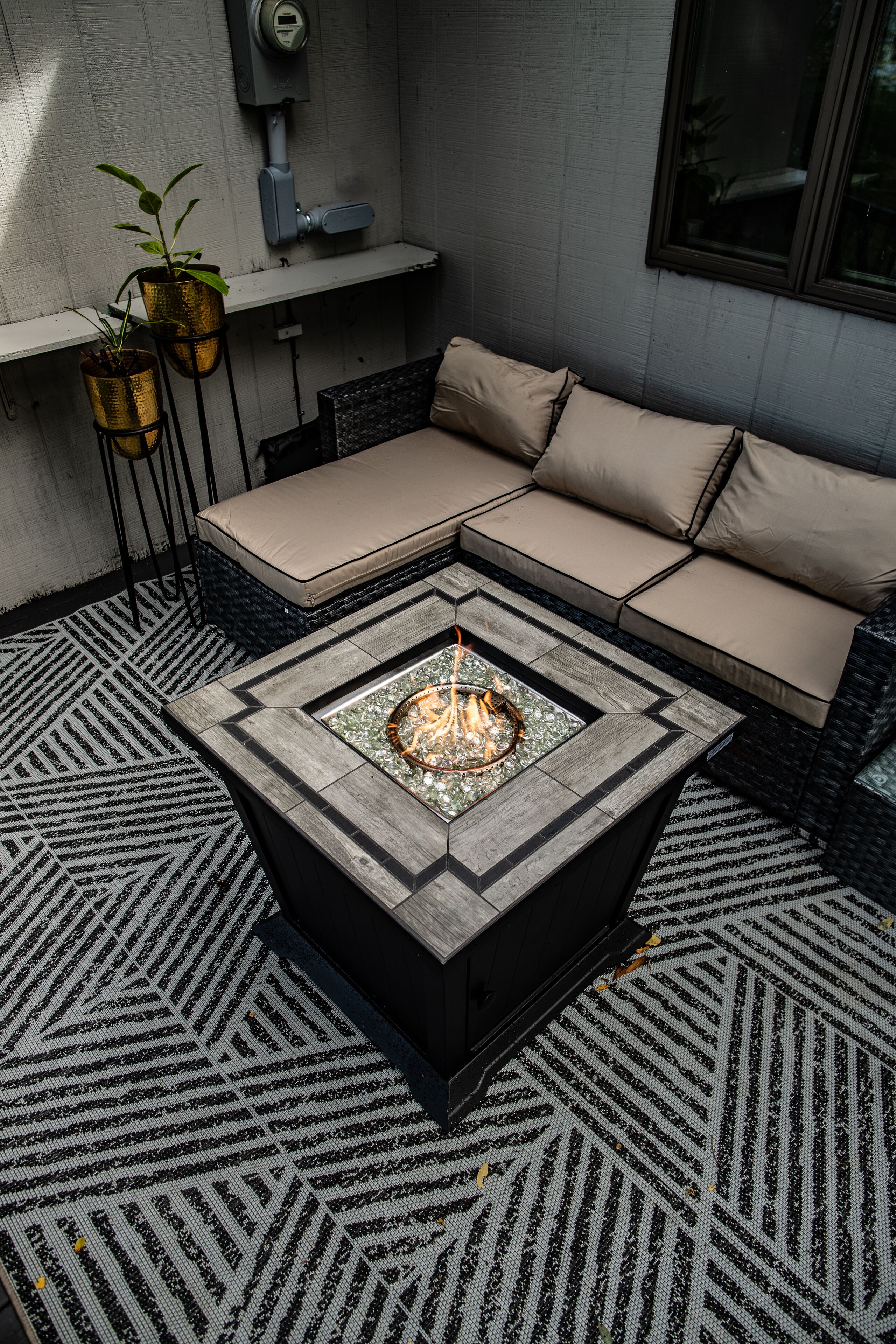 A modern outdoor seating area with a fire feature, patterned rug, and potted plants.