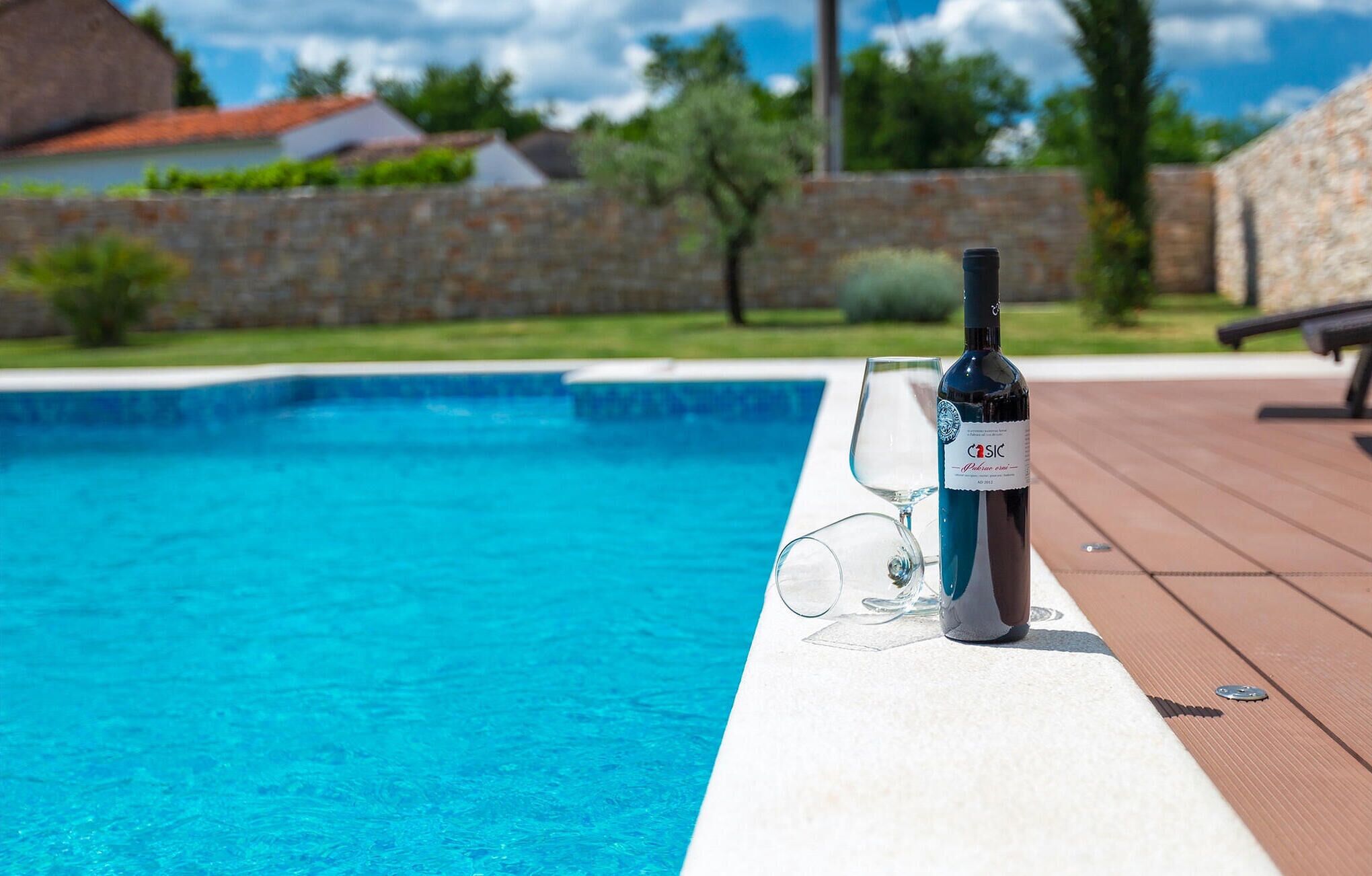 A poolside setting with a bottle of Casic wine, a glass, and a wooden deck.