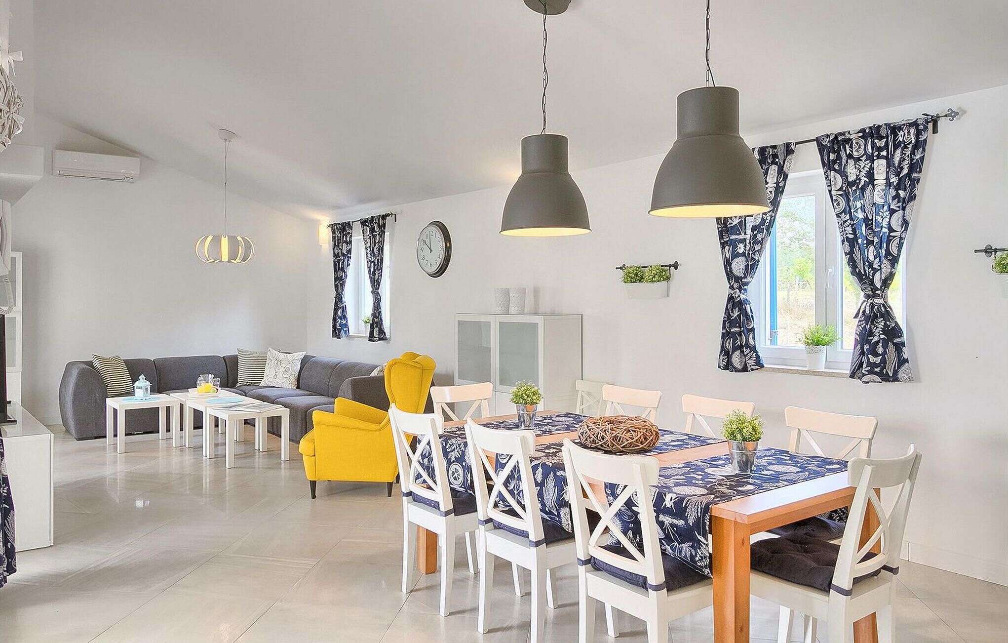 A modern living room with a sofa, yellow armchair, dining table with white chairs, and pendant lights.