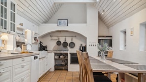 Una cocina moderna con armarios blancos, una isla grande y un comedor con mesa y sillas de madera.