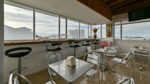 A dining area with metal chairs and tables, large windows with a view of buildings, and a wooden ceiling. - Hotel Grand Caribe (San Andrés)