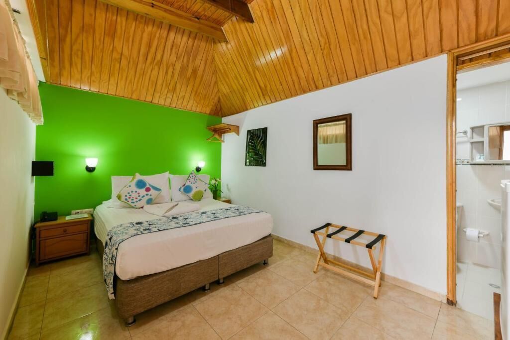 A bedroom with a bed, bedside tables, a bench, and a green wall.