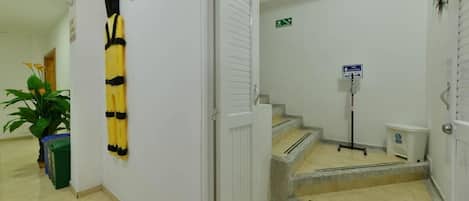 A clean, well-lit hallway with a staircase leading to an upper floor. There are signs indicating directions and a trash bin near the stairs.