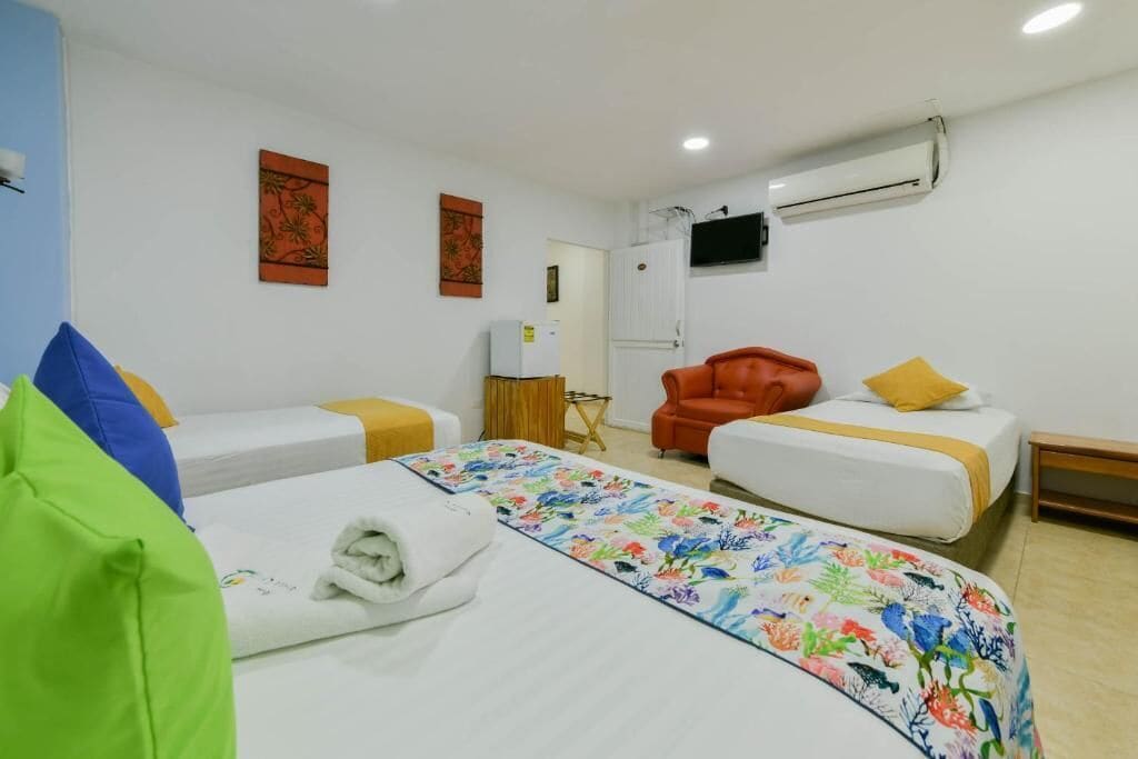 A hotel room with two beds, a TV mounted on the wall, and an air conditioning unit.