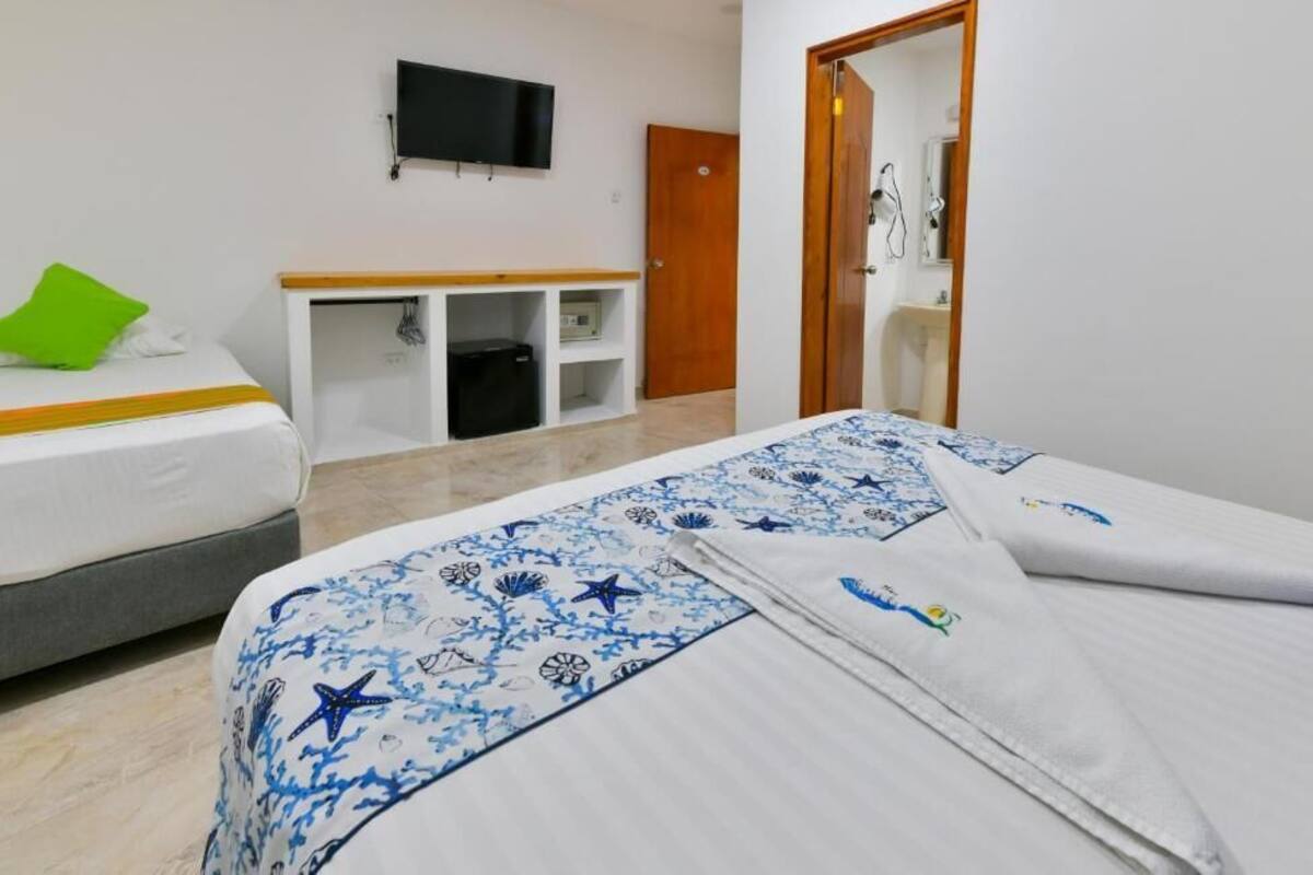 Habitación de hotel con dos camas, un televisor en la pared, un escritorio con una silla y una puerta que da al baño.