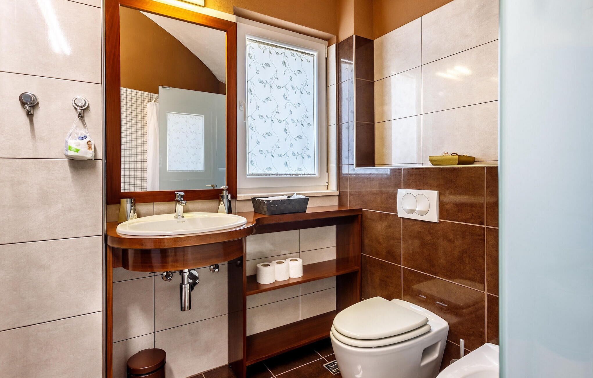 Une salle de bain équipée d’un lavabo, d’un miroir, de toilettes et d’une étagère contenant des articles de toilette.