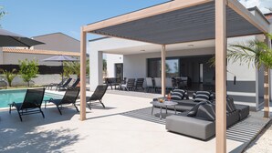 Ein überdachter Außenbereich mit Liegestühlen und einem Pool.