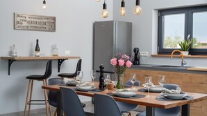Eine moderne Küche mit Essbereich, ausgestattet mit einem Holztisch für vier Personen, schwarzen Stühlen, einem Edelstahlkühlschrank und einem Fenster mit Aussicht.