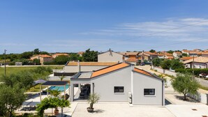 Ein modernes Haus mit Pool, einer überdachten Terrasse und Blick auf eine Wohngegend mit ähnlichen Häusern.