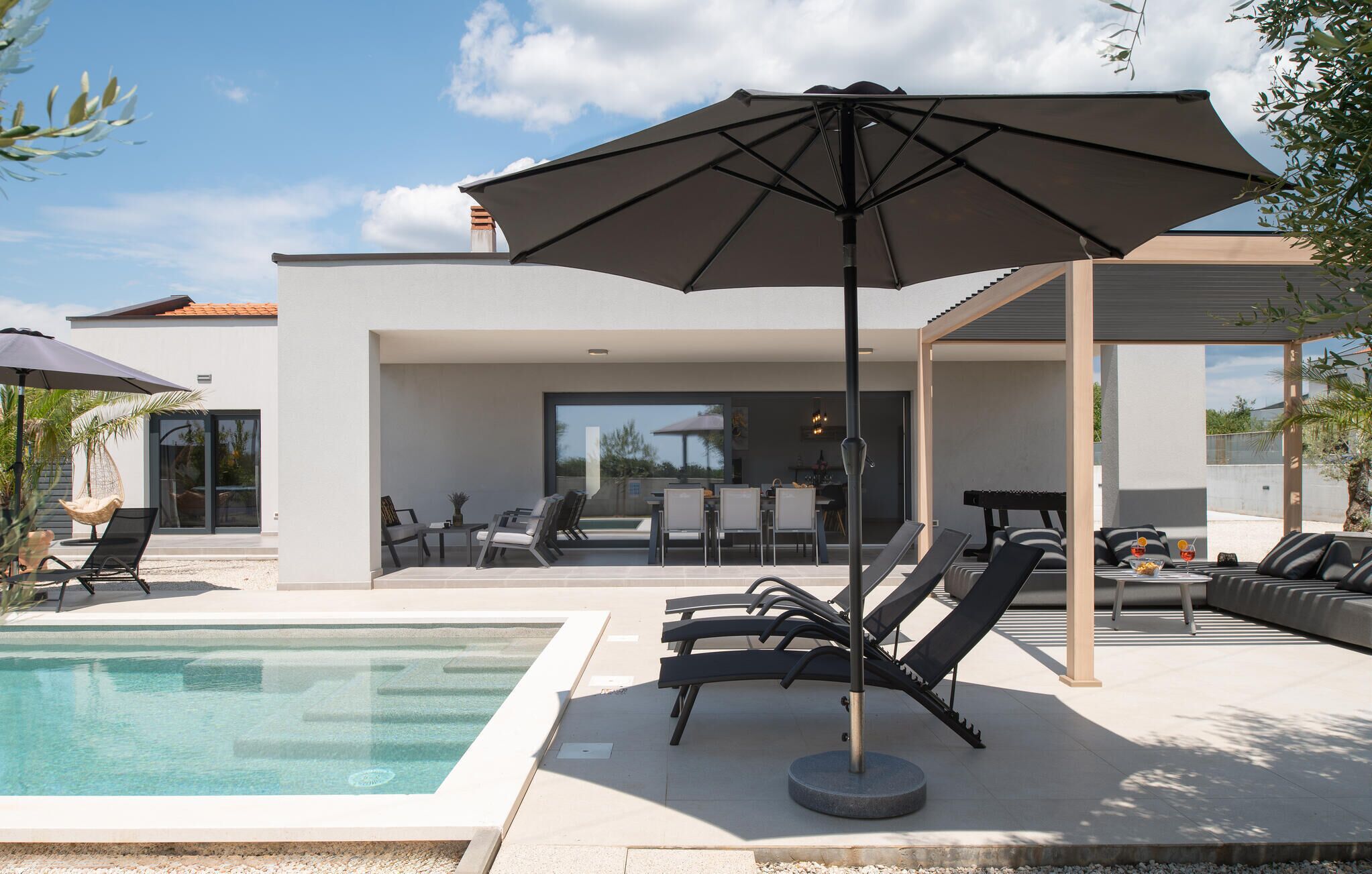 A modern outdoor pool area with lounge chairs and an umbrella.