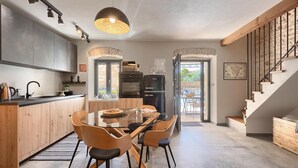 A modern kitchen with wooden cabinets, a black refrigerator, and a dining area with a glass table and wooden chairs.