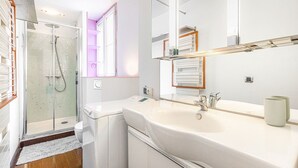 Une salle de bain moderne avec une douche à l’italienne en verre, un lavabo blanc et un grand miroir.