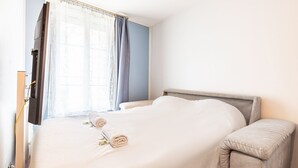 Un lit bien fait, avec une serviette pliée et un oreiller, une table de chevet et une fenêtre avec des rideaux.