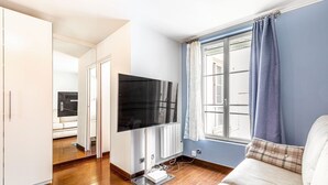 Un salon moderne avec un téléviseur à écran plat, un canapé et une fenêtre avec des rideaux.