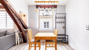 Una habitación acogedora con una mesa de madera, dos sillas, un sofá gris y un ventanal con vistas a edificios.