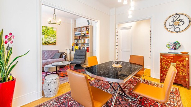 Uma área de refeições com mesa de mármore preto, cadeiras laranja e um tapete estampado vermelho.