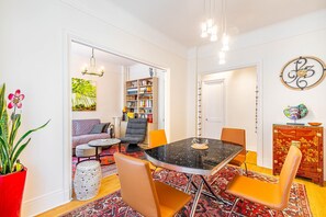 Uma área de refeições com mesa de mármore preto, cadeiras laranja e um tapete estampado vermelho.