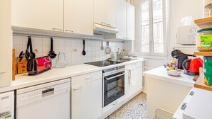 Uma cozinha moderna com armários brancos, lava-louças, forno e janela que proporciona iluminação natural.