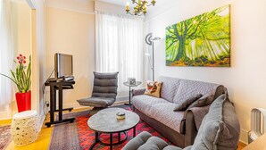 Sala de estar com sofá, poltronas, mesa de centro, televisão, pintura e planta em vaso.